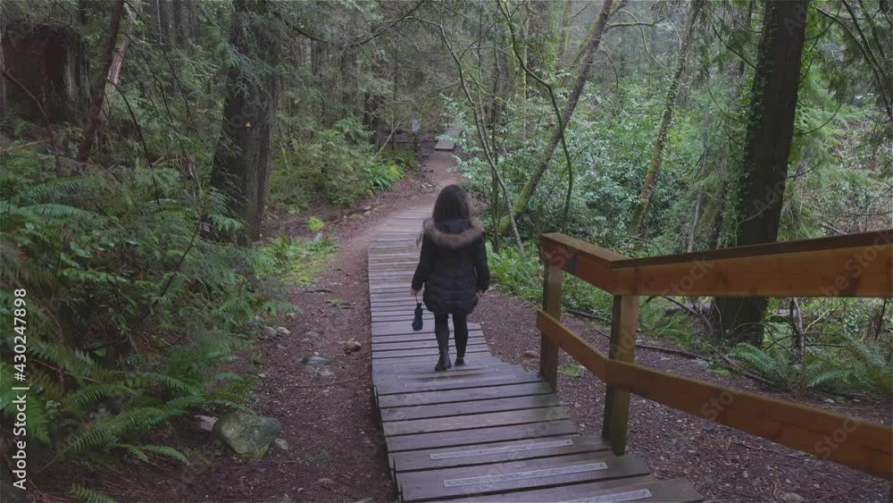 Girl Walking on a Beautiful Path in the Rainforest during a wet and rainy day. Lynn Canyon Park, North Vancouver, British Columbia, Canada. Girl Walking on a Beautiful Path in the Rainforest during a wet and rainy day. Lynn Canyon Park, North Vancouver, British Columbia, Canada.