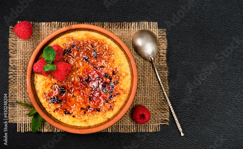 Obraz na plátně Creme brulee dessert of cream and cane sugar with fresh raspberries and mint leaves on a dark table, layout with copy space