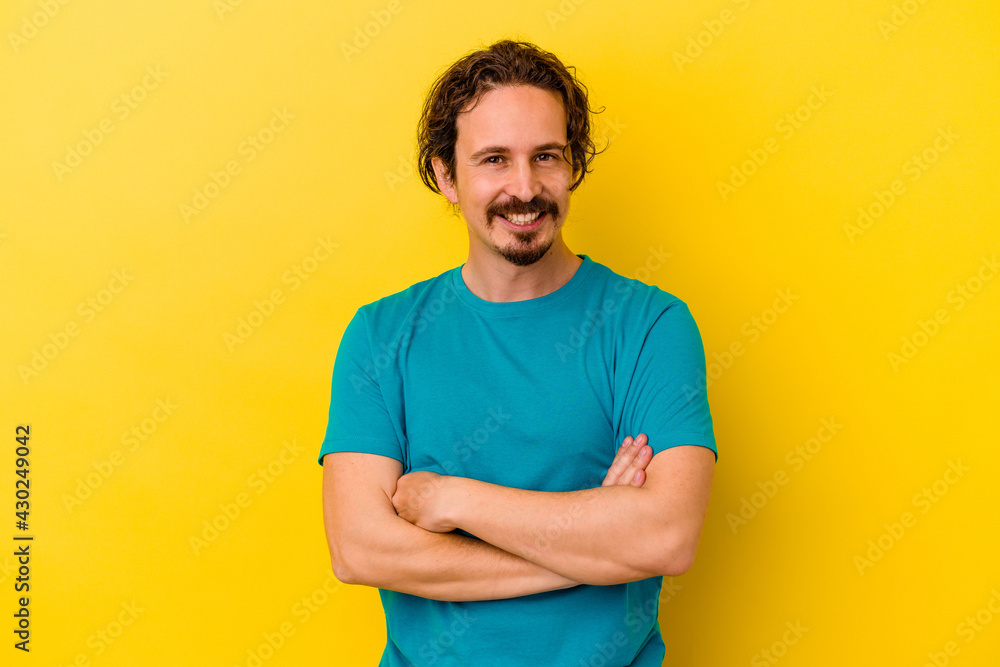 Young caucasian man isolated on yellow background who feels confident, crossing arms with determination. Young caucasian man isolated on yellow background who feels confident, crossing arms with determination.