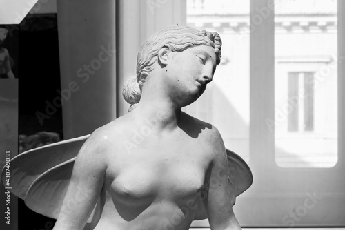 Black and white photo of marble sculpture representing a young woman posing with naked breasts