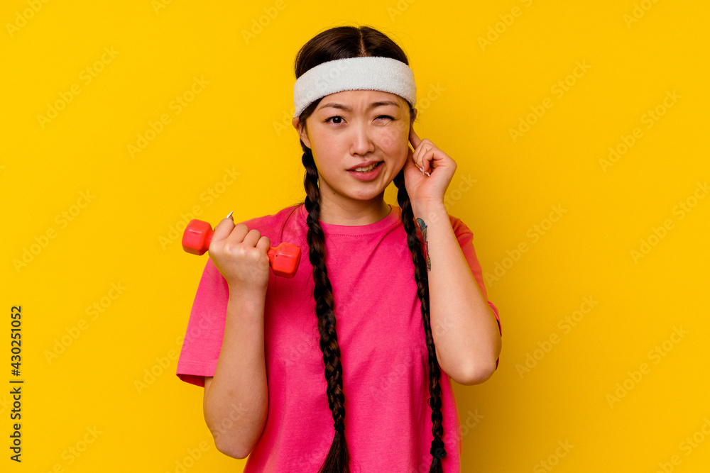 Young sport chinese woman isolated on yellow background covering ears with hands. Young sport chinese woman isolated on yellow background covering ears with hands.