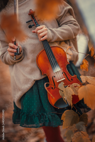 A beautiful girl with a violin in her hands among the autumn orange foliage in the forest and with music sheets in the background.