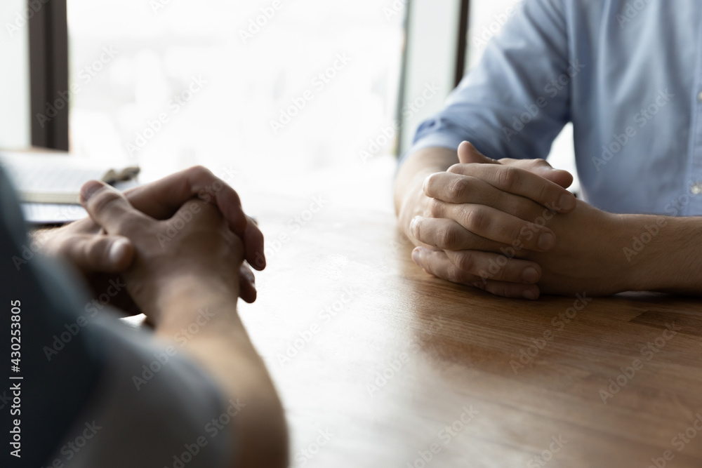 © fizkes - Crop close up of male business partners sit at desk with hands clasped talk at meeting in office. Businessmen or opponents face each other at business negotiation at workplace. Rivalry concept.