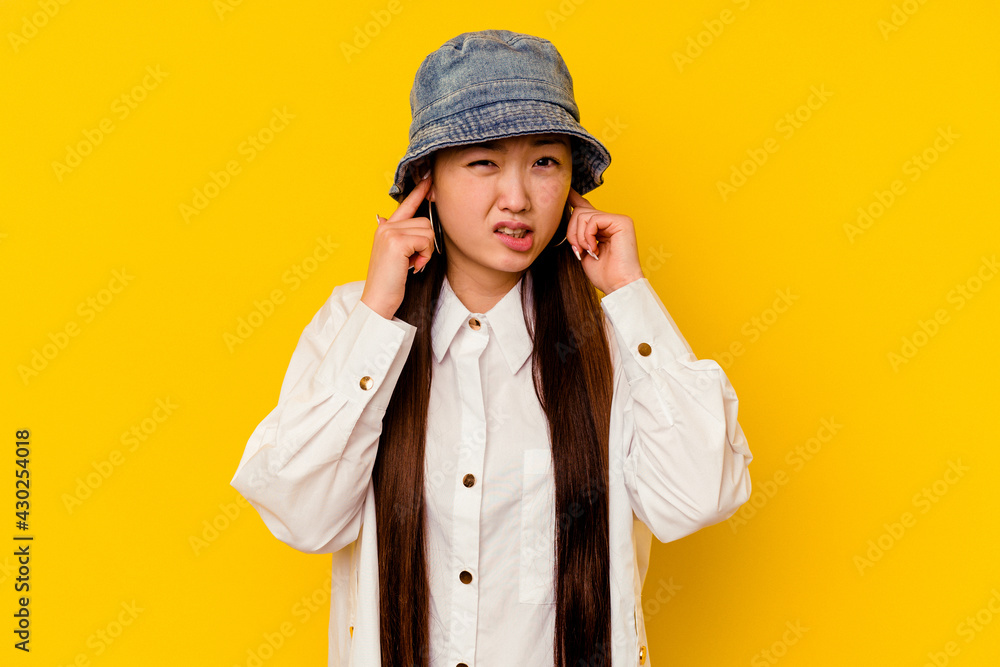 Young chinese woman isolated on yellow background covering ears with fingers, stressed and desperate by a loudly ambient. Young chinese woman isolated on yellow background covering ears with fingers, stressed and desperate by a loudly ambient.