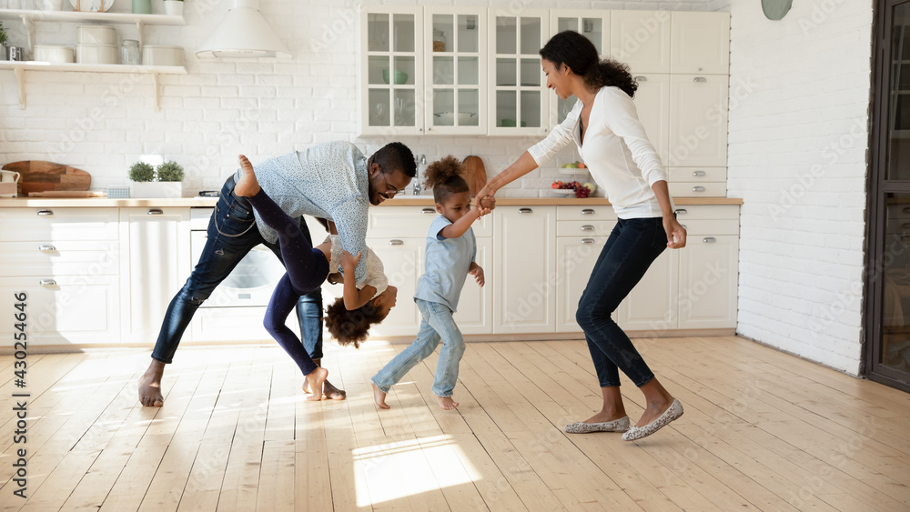 Excited African American family celebrating moving into new house. Happy parents and kids dancing in big modern kitchen interior, playing active games, exercising, having fun together at home party Excited African American family celebrating moving into new house. Happy parents and kids dancing in big modern kitchen interior, playing active games, exercising, having fun together at home party