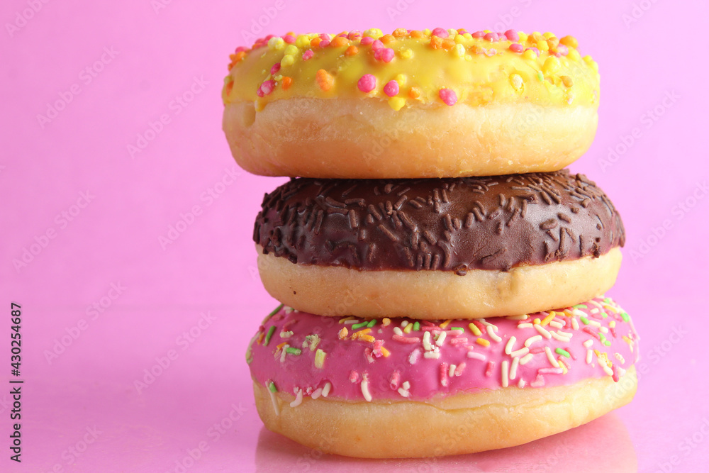 three Berliners donut pink yellow chocolate with a sprinkle on a pink background leit stack on top of each other with a place for text and with a copyspace three Berliners donut pink yellow chocolate with a sprinkle on a pink background leit stack on top of each other with a place for text and with a copyspace