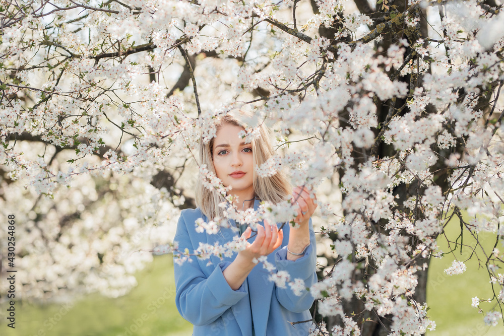 A beautiful girl stands under a flowering tree and holds a branch with flowers A beautiful girl stands under a flowering tree and holds a branch with flowers