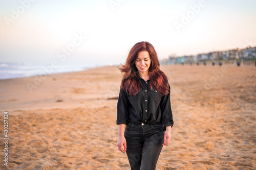 Beautiful young woman with long hair walks on the sand at Manhattan Beach in the early morning, Los Angeles