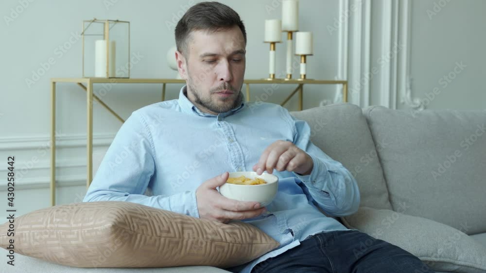 Man sits on the couch and eats potato chips Man sits on the couch and eats potato chips