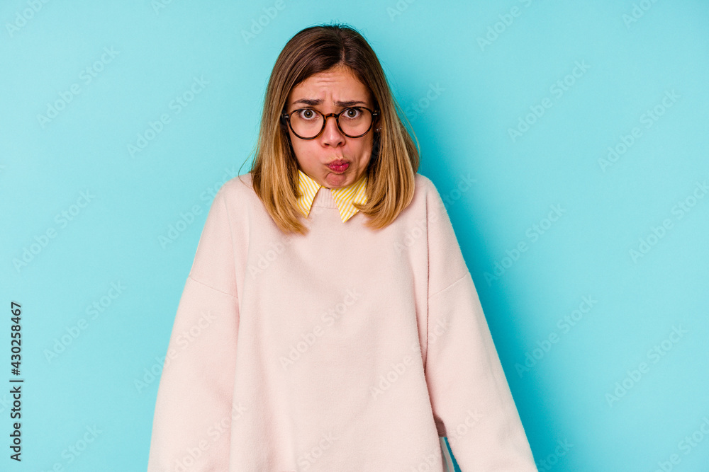 Fototapeta premium Young student caucasian woman isolated on blue background blows cheeks, has tired expression. Facial expression concept.