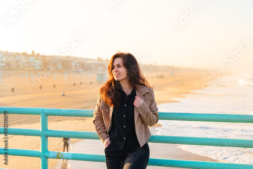 A young woman in a jacket stands on a pier overlooking the beach in the early morning, Los Angeles, California