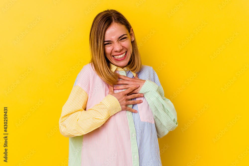 Young caucasian skinny woman isolated on yellow background laughs happily and has fun keeping hands on stomach. Young caucasian skinny woman isolated on yellow background laughs happily and has fun keeping hands on stomach.