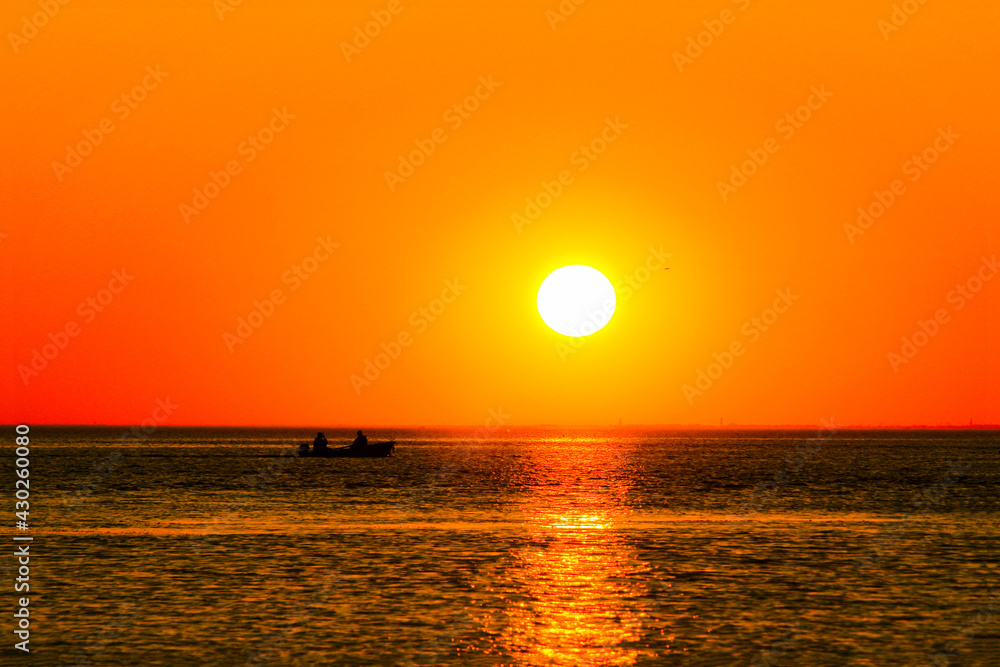 setting sun over the sea with reflection in the water and a sailing boat