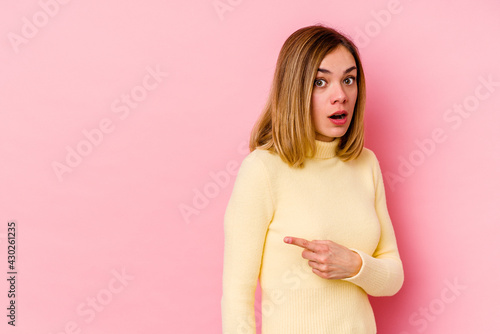 Young caucasian woman isolated on pink background smiling and pointing aside, showing something at blank space.