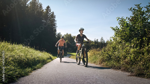 Mother and daughter riding mountain bikes in the country road in green nature on a sunny day.