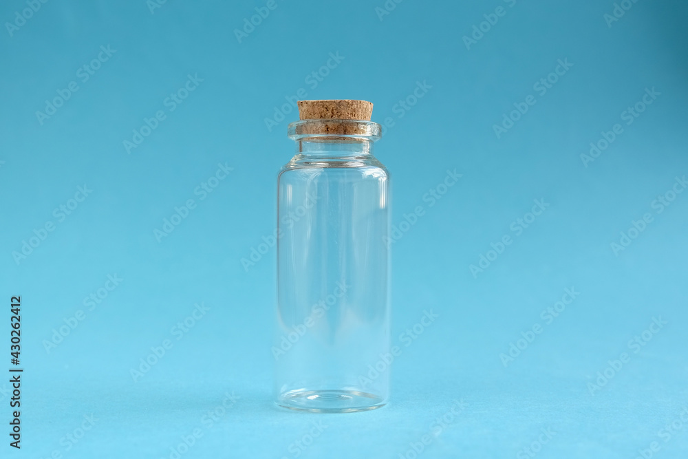Empty glass bottle with cork cap on blue background. Close-up, horizontal photo. Empty glass bottle with cork cap on blue background. Close-up, horizontal photo.