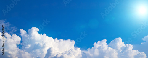 Blue sky background with white puffy clouds on a bottom foreground. Wide shot with cumulus clouds and cold blue sun. Banner, copy space, blank space for text photo