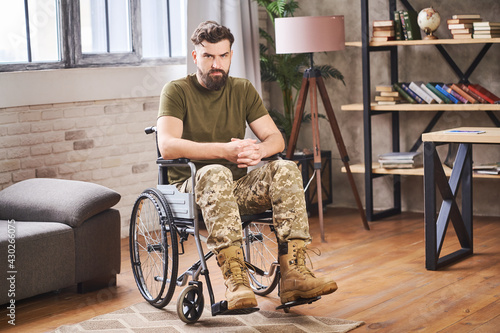 Young bearded disabled veteran sitting in a wheelchair and looking at the camera photo