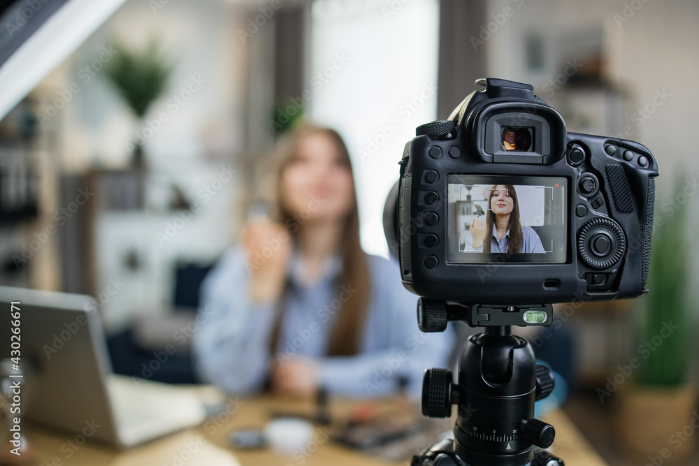 Charming caucasian woman using modern camera for filming online tutorial about new cosmetics. Young blogger sharing with skin care treatments in social network.