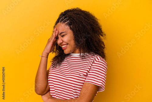 Young african american woman isolated on yellow background blink at the camera through fingers, embarrassed covering face.