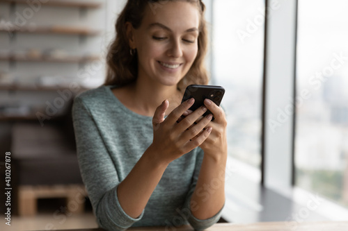 Crop close up of smiling millennial Caucasian woman hold smartphone text message on modern device online. Happy young female look at cellphone screen browse wireless internet. Technology concept.