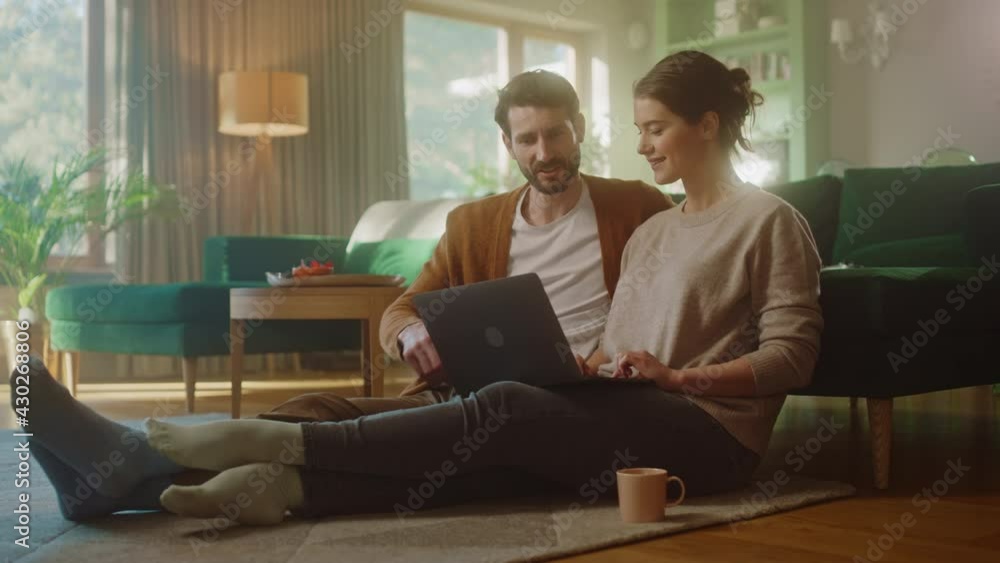 Couple Use Laptop Computer, while Sitting on the Living Floor room of their Apartment. Boyfriend and Girlfriend Talk, Shop on Internet, Choose Product to Order Online, Doing Remote Work Together Couple Use Laptop Computer, while Sitting on the Living Floor room of their Apartment. Boyfriend and Girlfriend Talk, Shop on Internet, Choose Product to Order Online, Doing Remote Work Together