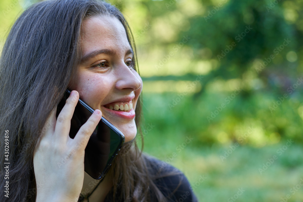 long-haired, fair-skinned woman sitting at a stone table with a coffee and her bag while talking on the phone, with green unfocused background. teenager in nature with his mobil taking a break. long-haired, fair-skinned woman sitting at a stone table with a coffee and her bag while talking on the phone, with green unfocused background. teenager in nature with his mobil taking a break.
