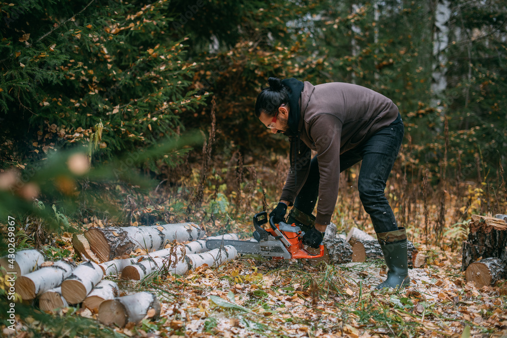 A man is sawing a tree with a chainsaw. A young guy works in a pine forest A man is sawing a tree with a chainsaw. A young guy works in a pine forest