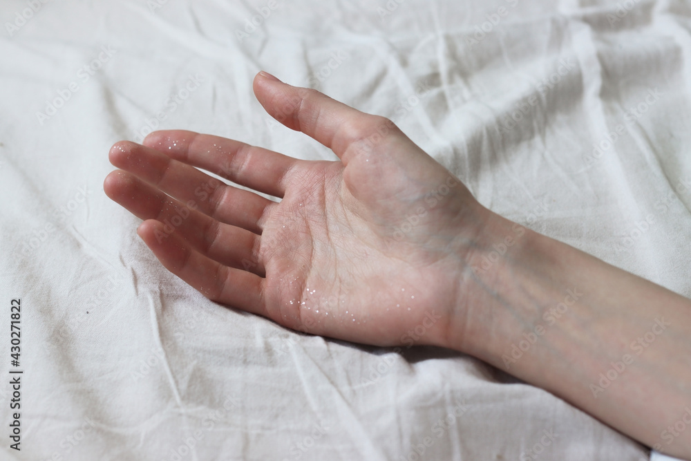 A woman graceful palm, stained with sequins, lies on a white sheet. Tenderness. Sleep aesthetics after a party. soft focus A woman graceful palm, stained with sequins, lies on a white sheet. Tenderness. Sleep aesthetics after a party. soft focus