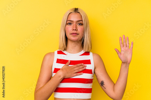 Young venezuelan woman isolated on yellow background taking an oath, putting hand on chest.