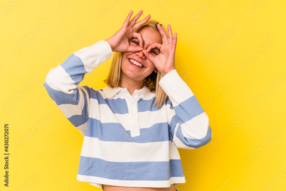 Young venezuelan woman isolated on yellow background showing okay sign over eyes Young venezuelan woman isolated on yellow background showing okay sign over eyes