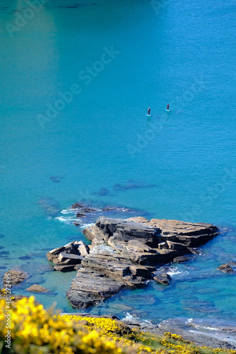 Two paddle boarders on the cornish coastline in perfect turquoise water.
