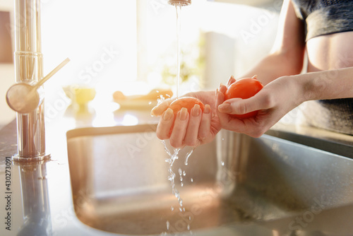 Fitness woman rinses fresh tomato in the sink photo