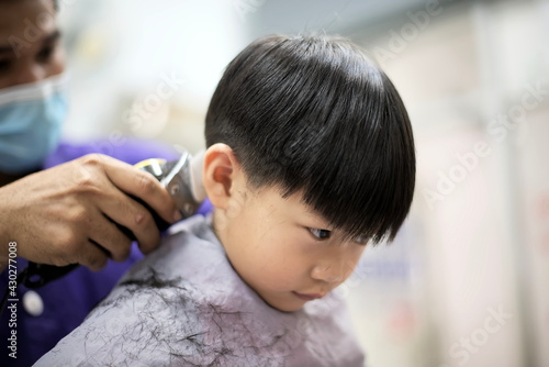 little boy is getting haircut by hairdresser at the barbershop