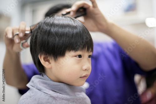 little asian boy is getting haircut by hairdresser at the barbershop
