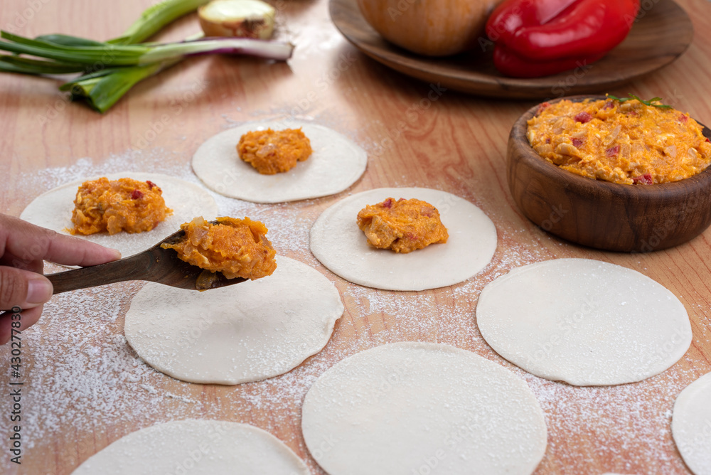 Empanadas tapas on wooden board and stuffed with vegetables and squash with bowl and flour preparation for Argentine empanadas Empanadas tapas on wooden board and stuffed with vegetables and squash with bowl and flour preparation for Argentine empanadas