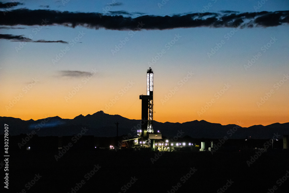 A oil and gas drilling/fracking operation and the front range of the Rocky Mountains, silhouetted by the sunset - East of Denver, Colorado