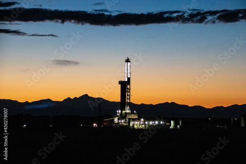 A oil and gas drilling/fracking operation and the front range of the Rocky Mountains, silhouetted by the sunset - East of Denver, Colorado photo