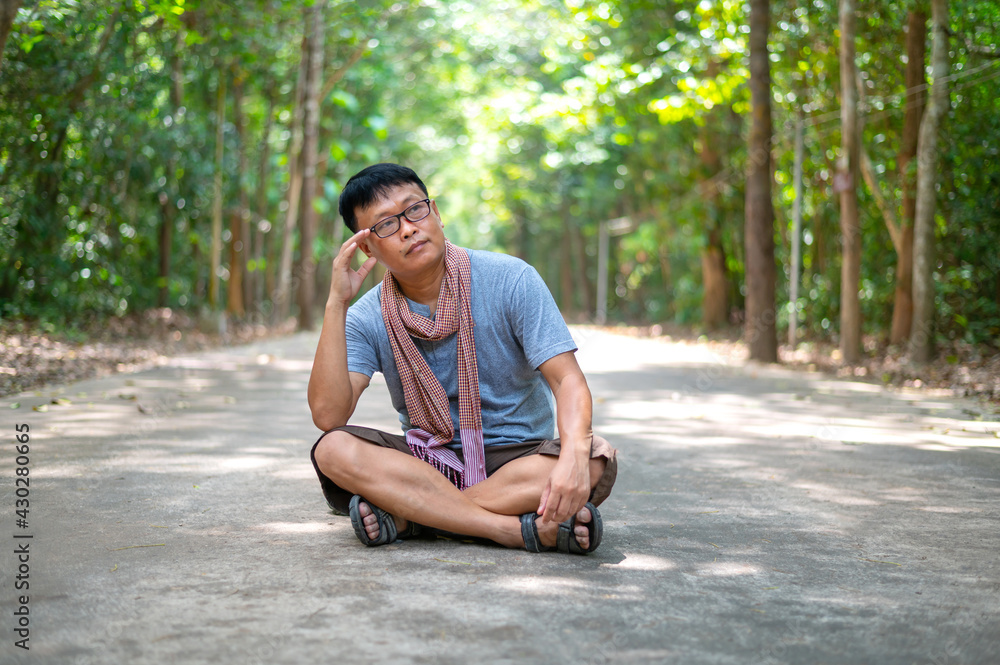Fototapeta premium Asian man sitting lonely in the park.Man relaxing in green natural park.Day dream working Asia people on summer vacation trip.