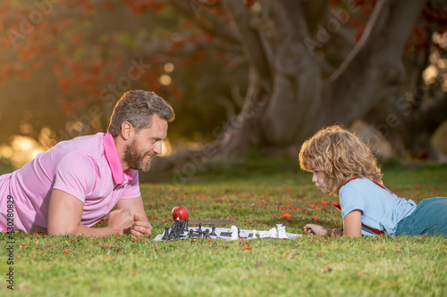 Happy family outdoor. Games and entertainment for children. Father and son playing chess in summer garden.