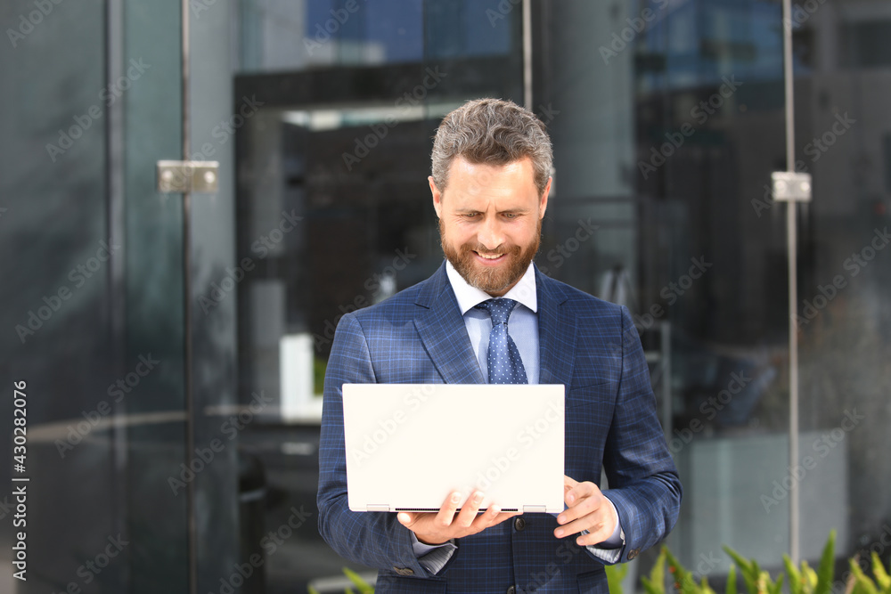 Business man holding laptop standing on the street near business office building. Business man holding laptop standing on the street near business office building.