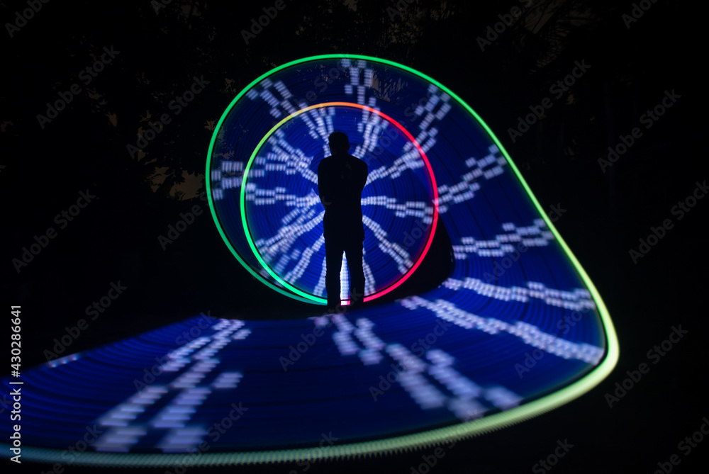 Obraz premium One person standing alone against a Colourful circle light painting as the backdrop 
