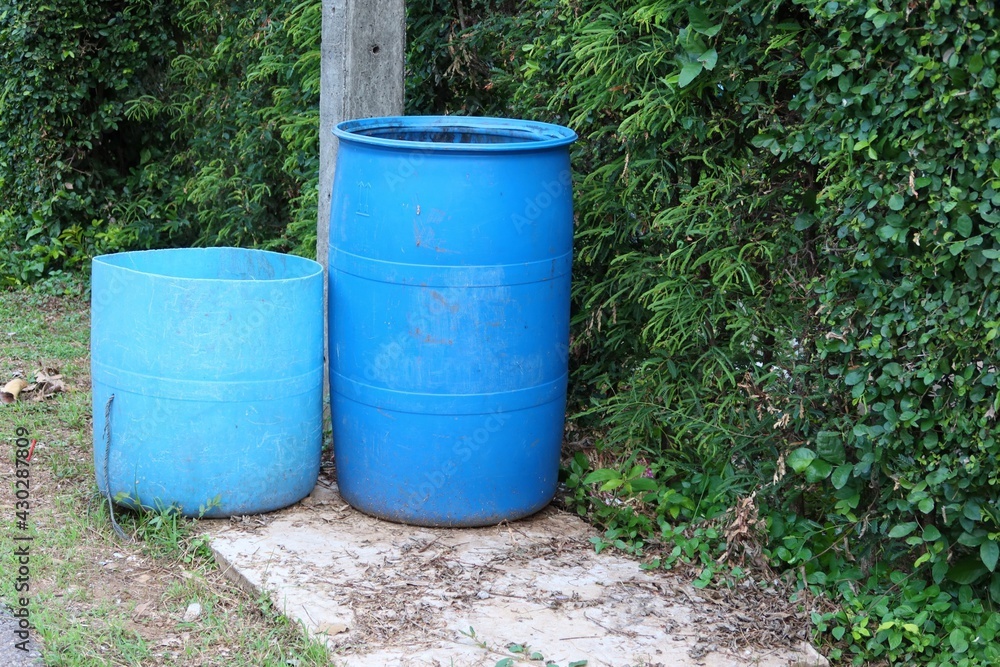 Two large blue plastic trash cans are located on an outdoor pavement area for littering. Two large blue plastic trash cans are located on an outdoor pavement area for littering.