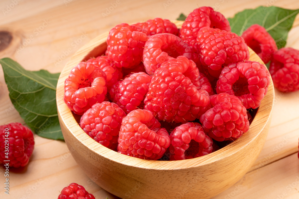 Raspberry fruit in tiny wooden bowl on Wooden background, Raspberries with leaves on Wooden background. Raspberry fruit in tiny wooden bowl on Wooden background, Raspberries with leaves on Wooden background.