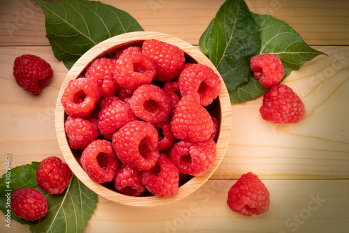 Raspberry fruit in tiny wooden bowl on Wooden background, Raspberries with leaves on Wooden background.
