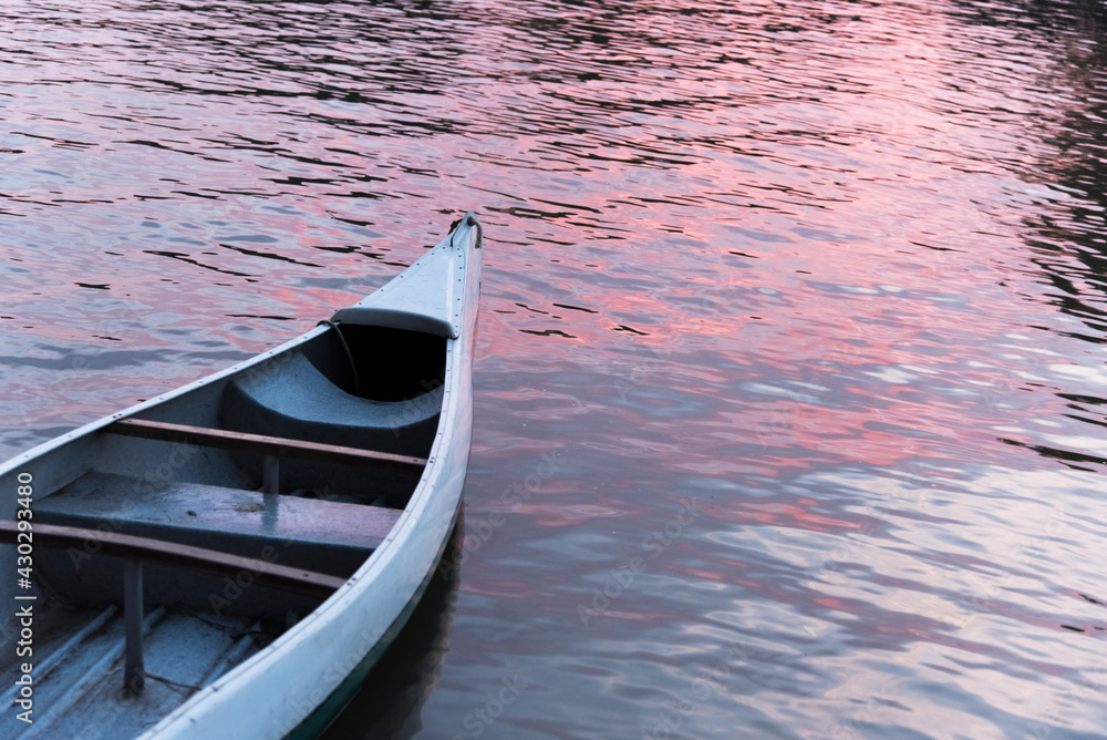 Canoe floating on a stream whose surface glows orange reflecting the sunset.