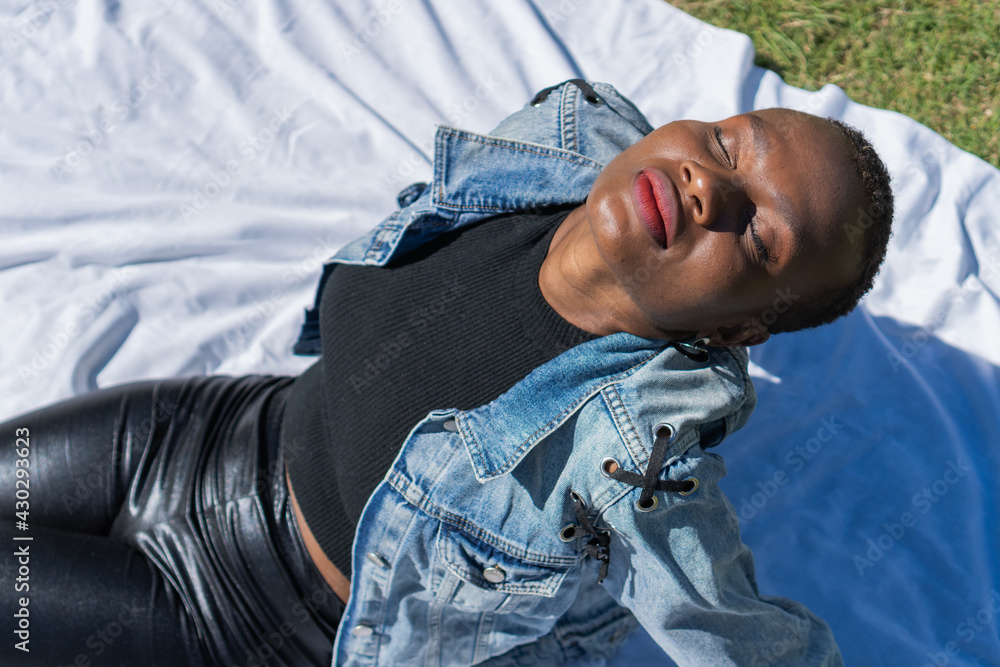 a black afro-american woman lying on a white blanket breathing in a park, with her eyes closed, relaxing expression, top view