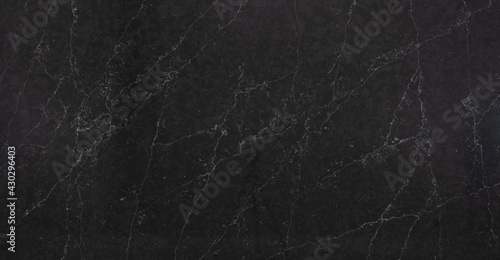 A dark marble looking quartz slab that contains a two-toned charcoal grey background with soft light grey subtle veins photo