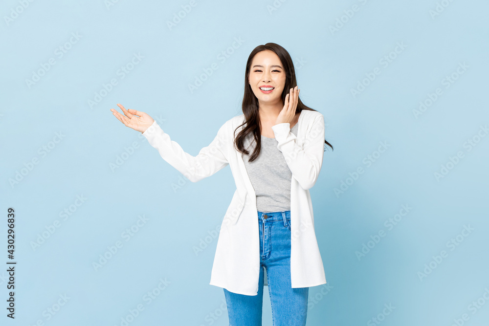 Smiling young pretty Asian woman with hands opening sideways in isolated light blue background Smiling young pretty Asian woman with hands opening sideways in isolated light blue background