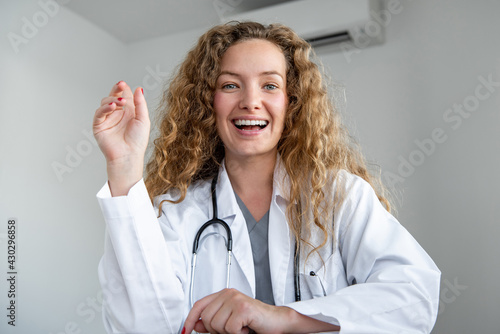 Cheerful smiling young female doctor looking at camera greeting patient online via video calling, home medical consulation service concepts photo